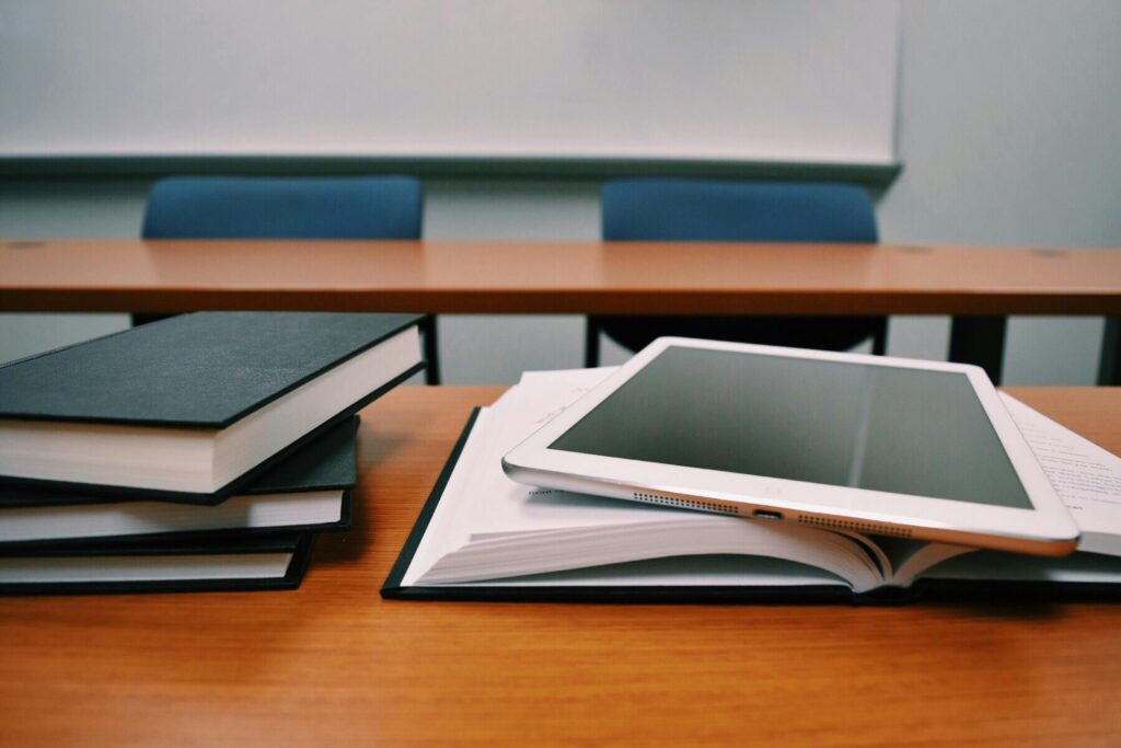 pexels-photo-289737-289737-1 Books and a tablet on a desk in a classroom, depicting modern education.